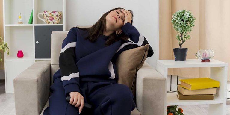 A woman sits in an armchair holding her forehead in distress, illustrating fatigue or mood swings linked to hormone imbalance.